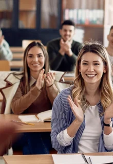 smiling, clapping students sitting in a college classroom